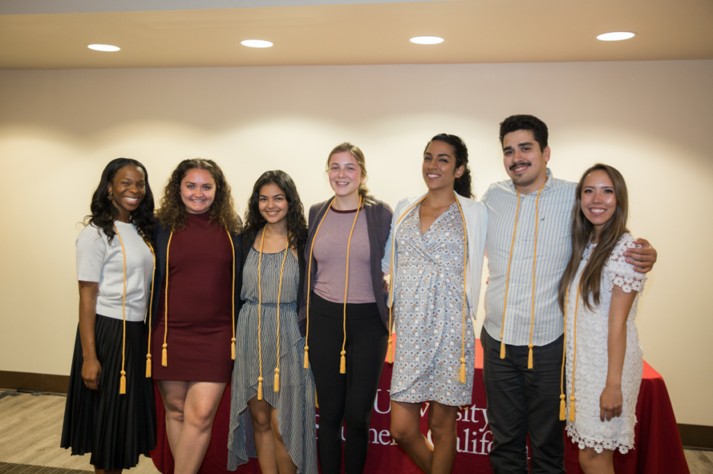 Seven students posing with graduation tassels